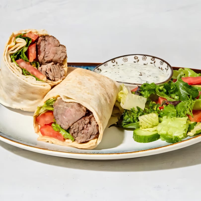 Two beef wraps with lettuce and tomato, served with a side salad and white sauce.