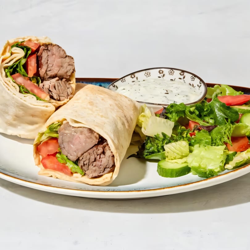 Two beef wraps with lettuce and tomato, served with a side salad and dipping sauce.