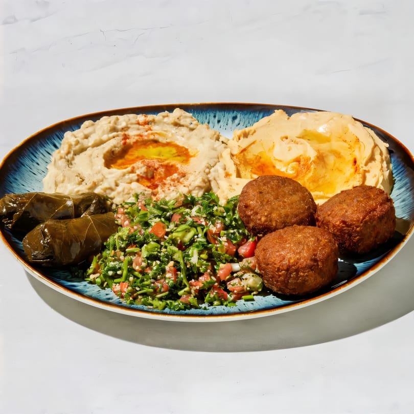 A blue plate with two servings of hummus, falafel, stuffed grape leaves, and tabbouleh salad.